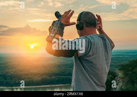 Uomo con ortosi regolabile del gomito articolato sulla scogliera in cima al tramonto Foto Stock