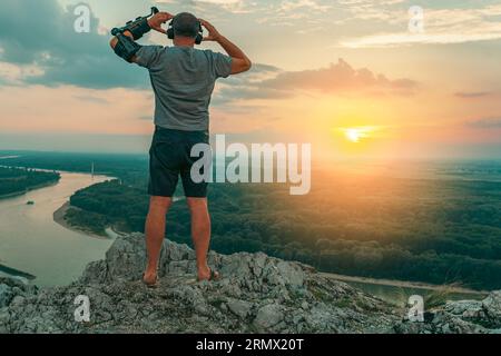 Uomo con ortosi regolabile del gomito articolato sulla scogliera in cima al tramonto Foto Stock