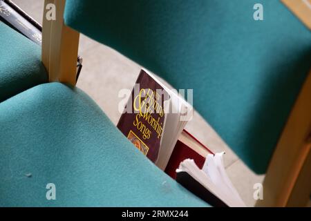 Un libro di inni e canti di culto sotto una sedia all'interno di una chiesa Foto Stock