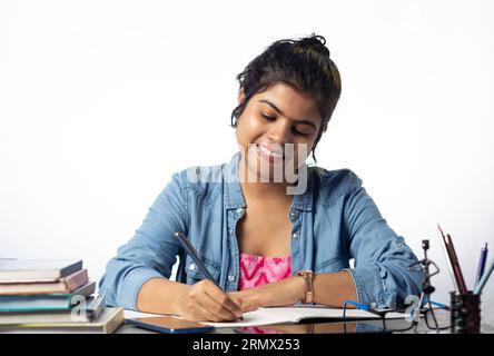 Un giovane studente indiano che studia e scrive su un tavolo da studio e su uno sfondo bianco Foto Stock