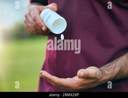 Scatola di pillole, medicina e uomo primo piano di mano di uno sport su un campo di calcio con tablet e farmaci per la salute. Supplementi, contenitore ed esterno con un Foto Stock