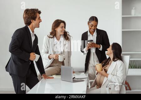 Felice donna in attesa latina che parla con i suoi colleghi d'affari multirazziali mentre fa una pausa in un ufficio moderno Foto Stock