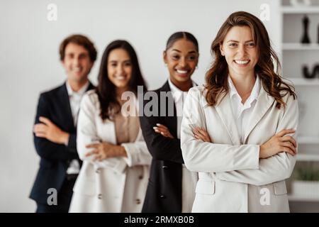 Team multietnico per gli affari. Gruppo di colleghi multiculturali con boss donna in posa in ufficio in piedi con le braccia piegate Foto Stock