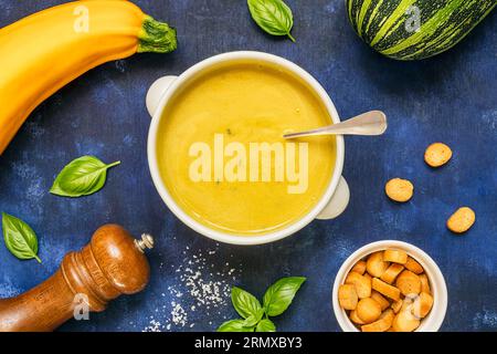 Zuppa vegetariana di zucchine fatta in casa in una ciotola bianca su sfondo blu, vista dall'alto Foto Stock