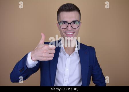 Sorridente giovane bell'uomo elegante con il gesto alzato del pollice su sfondo isolato Foto Stock