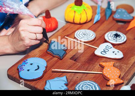 Le mani delle donne decorano il pan di zenzero come un dolce regalo di Halloween per i bambini. Prepararsi per la festa di Halloween. Foto Stock