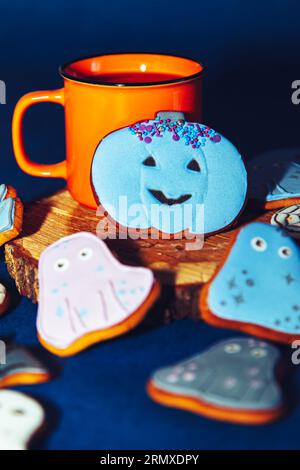 Biscotti di Halloween dipinti con pan di zenzero e una tazza arancione su sfondo blu. Sfondo gastronomico di Halloween. Foto Stock