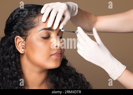 Cosmetologist making botox injection in interbrow zone to latin chubby woman getting anti-wrinke treatment, closeup Foto Stock