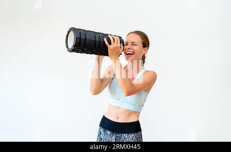 L'istruttrice di fitness femminile si diverte a usare il rullo di fitness in schiuma come un bicchiere di spioncino. Foto Stock