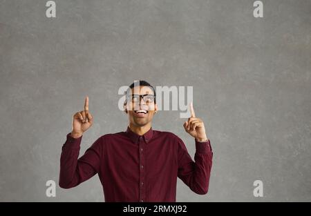 Eccitato giovane uomo afro-americano casual che indossa occhiali che puntano le dita verso l'alto Foto Stock