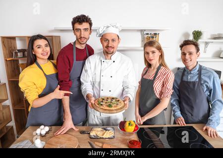 Italian chef with prepared pizza and group of young people after cooking class in kitchen Stock Photo