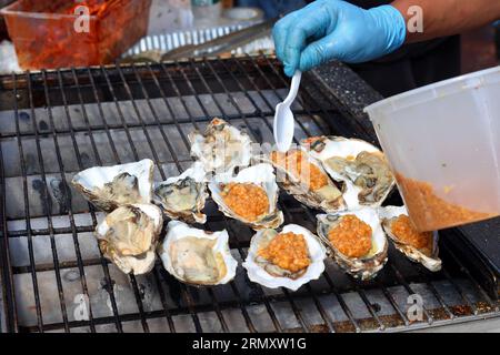 Ji Xiang BBQ Cook prepara ostriche grigliate sulla mezza conchiglia al Dragon Fes food festival Street Fair sulla 4th Avenue a New York City, 27 agosto 2023. Foto Stock