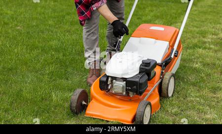 L'uomo irriconoscibile del giardiniere nei guanti di protezione avvia il rasaerba prima di tagliare il prato verde nel suo cortile. Uomo con rasaerba motorizzato ca Foto Stock