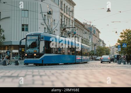 Tram pubblico blu nella città di Cracovia, in Polonia, la sera di inizio estate, pedalando per le strade della città trafficata. Tram moderno nella città polacca. Foto Stock