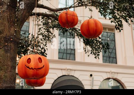 Zucca luminosa con una spaventosa faccia di Halloween appesa su un albero con ghirlande. Sfondo del poster delle festività Foto Stock