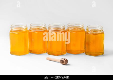 Composizione concettuale di barattoli di miele sotto forma di favi a nido d'ape e immersione in legno in isolamento. Vaschette di vetro aperte della stessa forma e dimensione Foto Stock