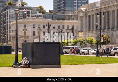 San Francisco, CA, USA - July 12, 2023: Homeless couple sleep on Civic Center Plaza in front of City Hall. Cars and pedestrians nearby Stock Photo