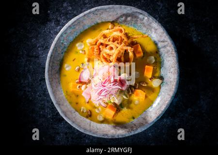 Vista dall'alto della gustosa zuppa di purea di zucca con pesce e cipolla fritta servita in ciotola su sfondo nero nel ristorante Foto Stock