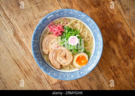 Vista dall'alto della deliziosa zuppa di ramen con uovo morbido bollito e maiale chashu servito in una ciotola di ceramica posta su un tavolo di legno Foto Stock