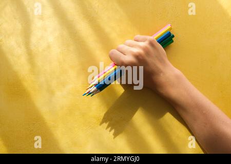 Pickinauna mano del bambino raccogliendo matite colorate su sfondo giallo . Foto di alta qualità Foto Stock