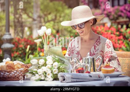 Foto di una donna che indossa occhiali da sole che si appresta a brunch in giardino. Foto Stock