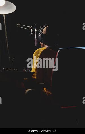 Vista posteriore di una donna anonima che parla in cuffie mentre lavora in uno studio di registrazione moderno e buio Foto Stock