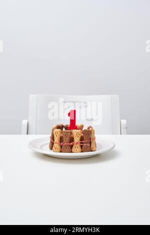 Appetitosa torta fatta in casa decorata con dolcetti ossei e candela rossa su piatto bianco posto vicino a una sedia vuota su un tavolo grigio Foto Stock