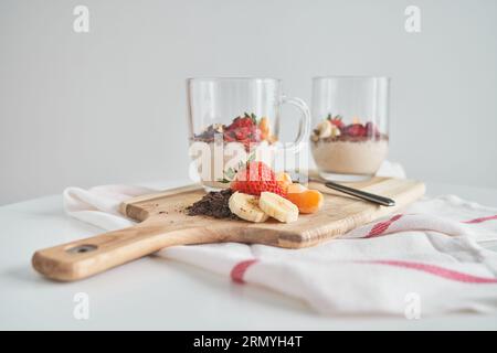 Composizione di yogurt fresco con cioccolato grattugiato e mandarino alla banana a fette e fragole poste su un tagliere su un tovagliolo bianco Foto Stock