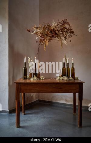 Interni retrò di un classico tavolo in legno con bottiglie di birra e vino con candele accese e bouquet di fiori secchi Foto Stock