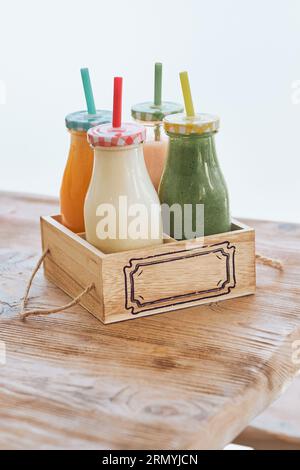 Frullati sani serviti in bottiglie di vetro con cannucce colorate in scatola su tavolo di legno Foto Stock