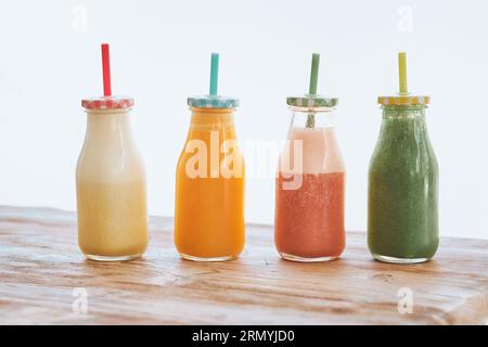 Bottiglie di vetro con cannucce colorate ripiene di frullati di frutta assortiti serviti su un tavolo di legno in fila in una stanza luminosa Foto Stock