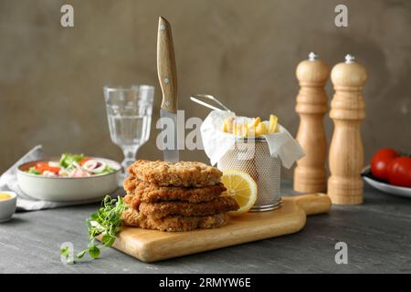 Tasty schnitzels served with knife and french fries on grey table Stock Photo