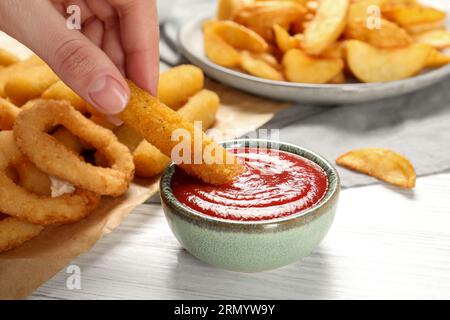 Donna che immerge il bastoncino di formaggio nel recipiente con il saporito ketchup al tavolo bianco, primo piano Foto Stock