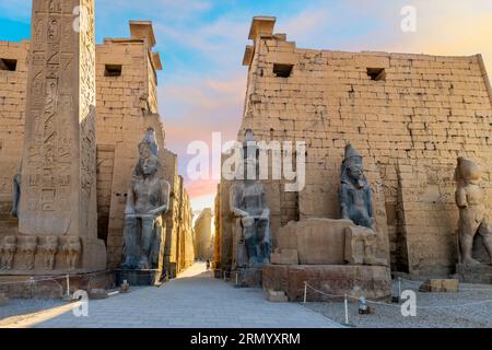 Ingresso all'antico tempio egizio di Luxor con statue di Ramses II e l'obelisco del pilone mentre il sole si trasforma nei colori vicino al tramonto a Luxor, in Egitto. Foto Stock
