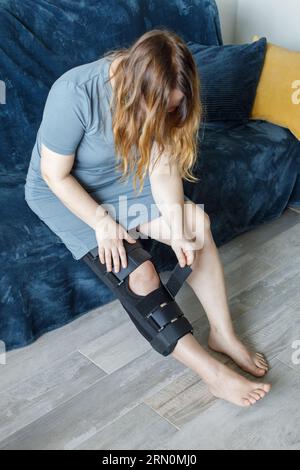 Donna con ginocchiere a casa. Ortopedic Anatomic Orthosis (Ortopedic Anatomic Orthosis). Apparecchi per fissaggio al ginocchio, lesioni e dolore Foto Stock
