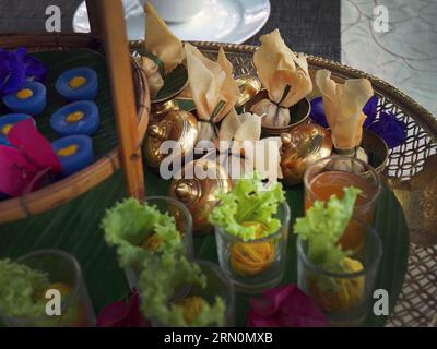 Snack thailandesi di vario tipo e colore su foglia di banana con motivo a tessitura in ottone metallo, fritto in profondità, croccante in una piccola tazza di ottone, ambientato come High Tea Foto Stock