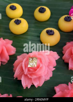 Snack dolci tailandesi di vario tipo e colore su foglia di banana con motivo intrecciato in ottone e metallo, ambientazione come tè pomeridiano o tè pomeridiano Foto Stock