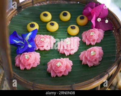 Snack dolci tailandesi di vario tipo e colore su foglia di banana con motivo intrecciato in ottone e metallo, ambientazione come tè pomeridiano o tè pomeridiano Foto Stock