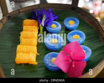 Snack dolci tailandesi di vario tipo e colore su foglia di banana con motivo intrecciato in ottone e metallo, ambientazione come tè pomeridiano o tè pomeridiano Foto Stock