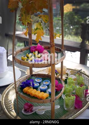 Snack dolci tailandesi di vario tipo e colore su foglia di banana con motivo intrecciato in ottone e metallo, ambientazione come tè pomeridiano o tè pomeridiano Foto Stock