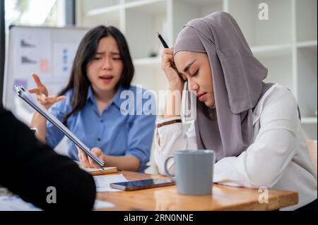 Una donna d'affari asiatica insoddisfatta e seria si lamenta degli errori del progetto al suo dipendente o collega musulmano durante l'incontro. Foto Stock