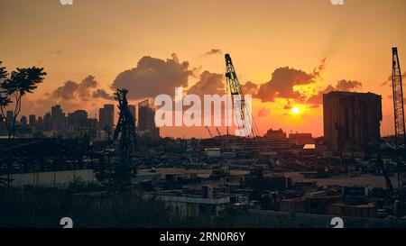 Porto di Beirut al tramonto. Elevatore della granella danneggiato, gru, contenitori di carico e detriti metallici attorcigliati ai raggi solari. Beirut, Libano - Maggio Foto Stock
