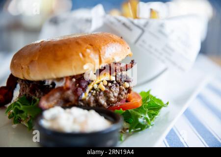 Hamburger appetitoso con verdure, patatine fritte e salsa al piatto servito al tavolo del caffè Foto Stock