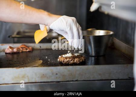 Lo chef cucina hamburger, friggendo carne di manzo in padella nella cucina del ristorante. Lavoratore di un fast food che prepara cotolette di maiale Foto Stock