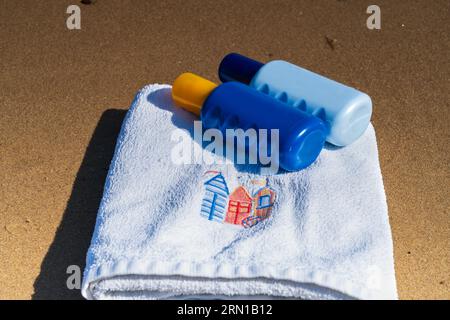 Beach towel and suntan spray bottles on the beach.  Summer holiday/vacation concept Stock Photo