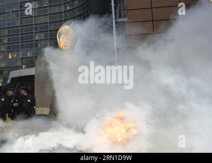 (141219) -- BRUXELLES, 19 dicembre 2014 -- la polizia belga si trova accanto a un'effigie della cancelliera tedesca Angela Merkel mentre i manifestanti del settore lattiero-caseario bruciano balle di fieno a un incrocio di fronte alla sede centrale dell'UE a Bruxelles, in Belgio, durante un movimento di protesta contro le politiche di austerità e il partenariato transatlantico per il commercio e gli investimenti (TTIP), 19 dicembre 2014. ) BELGIO-BRUXELLES-UE-AGRICOLTORI-LATTIERO-CASEARI-DIMOSTRAZIONE YexPingfan PUBLICATIONxNOTxINxCHN Bruxelles DEC 19 2014 la polizia belga si trova accanto all'effigie della cancelliera tedesca Angela Merkel come dimostratore del settore caseario Burn Bales of Hay AT a Cross Road in Front of T. Foto Stock