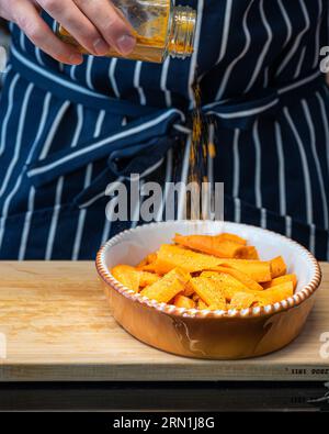 lo chef condisce le carote a fette in un recipiente prima di metterle in forno e il grembiule sullo sfondo Foto Stock