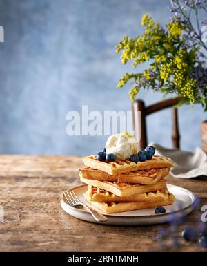 Waffle conditi con mirtilli, gelato e miele su un rustico tavolo marrone. Sfondo blu. Calma la natura morta con spazio extra. Minimalista Foto Stock