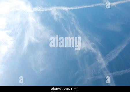 Nuvole di Cirrus e lunghe file di sentieri per aerei. L'aereo aeroplano si contraglia con lo sfondo blu del cielo nuvoloso. Linea orizzontale di volo aereo veloce in dista Foto Stock