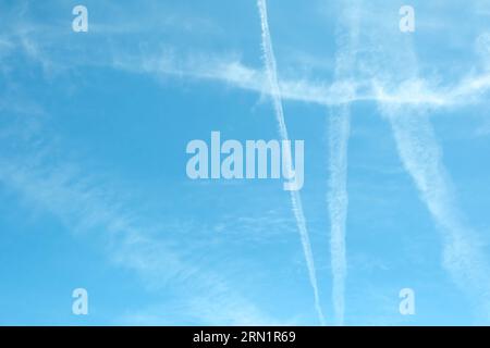 Nuvole di Cirrus e lunghe file di sentieri per aerei. L'aereo aeroplano si contraglia con lo sfondo blu del cielo nuvoloso. Linea orizzontale di volo aereo veloce in dista Foto Stock